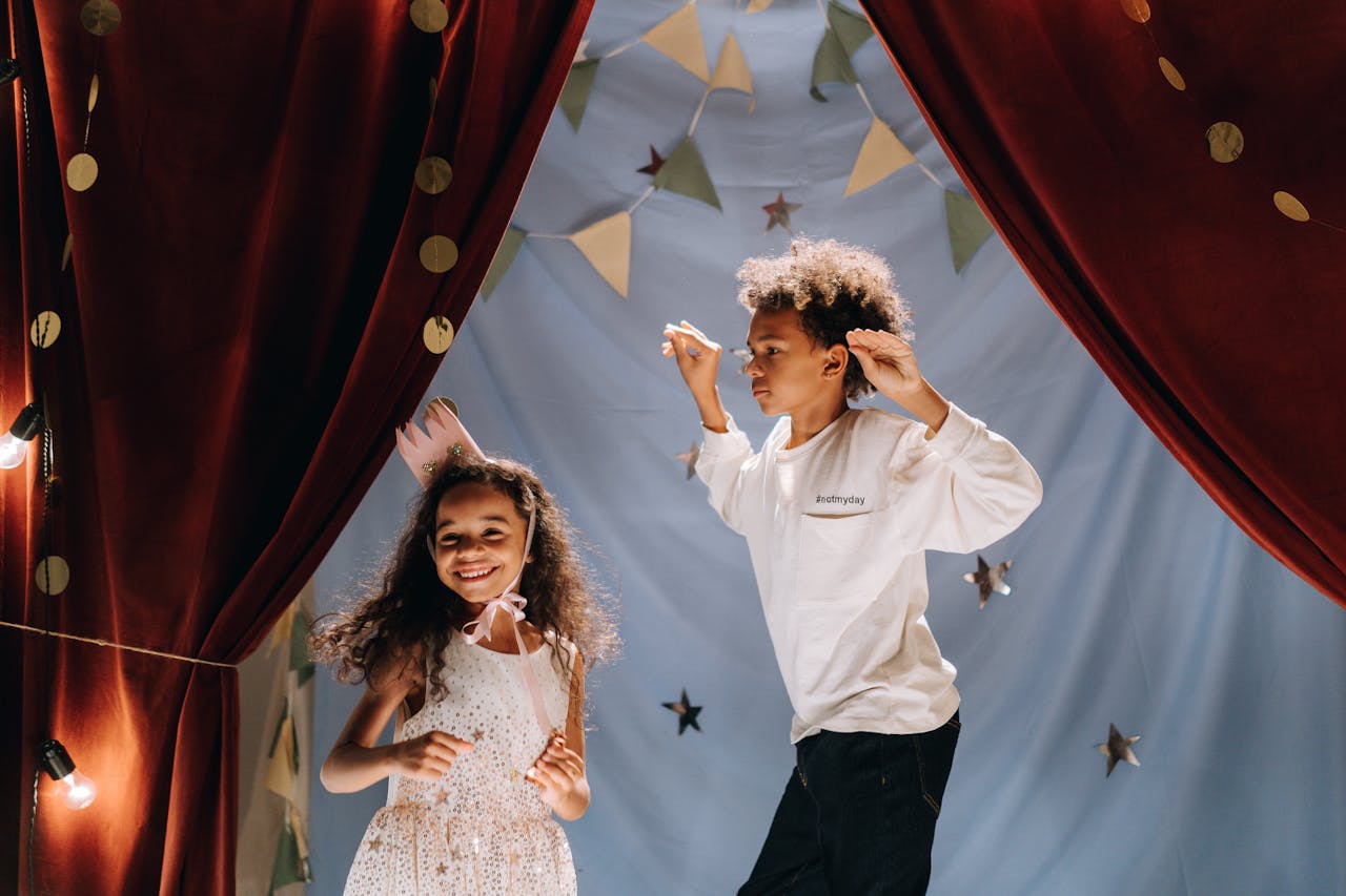 Two joyful kids performing in a homemade theater setup with costumes and curtains, having a fun time indoors.