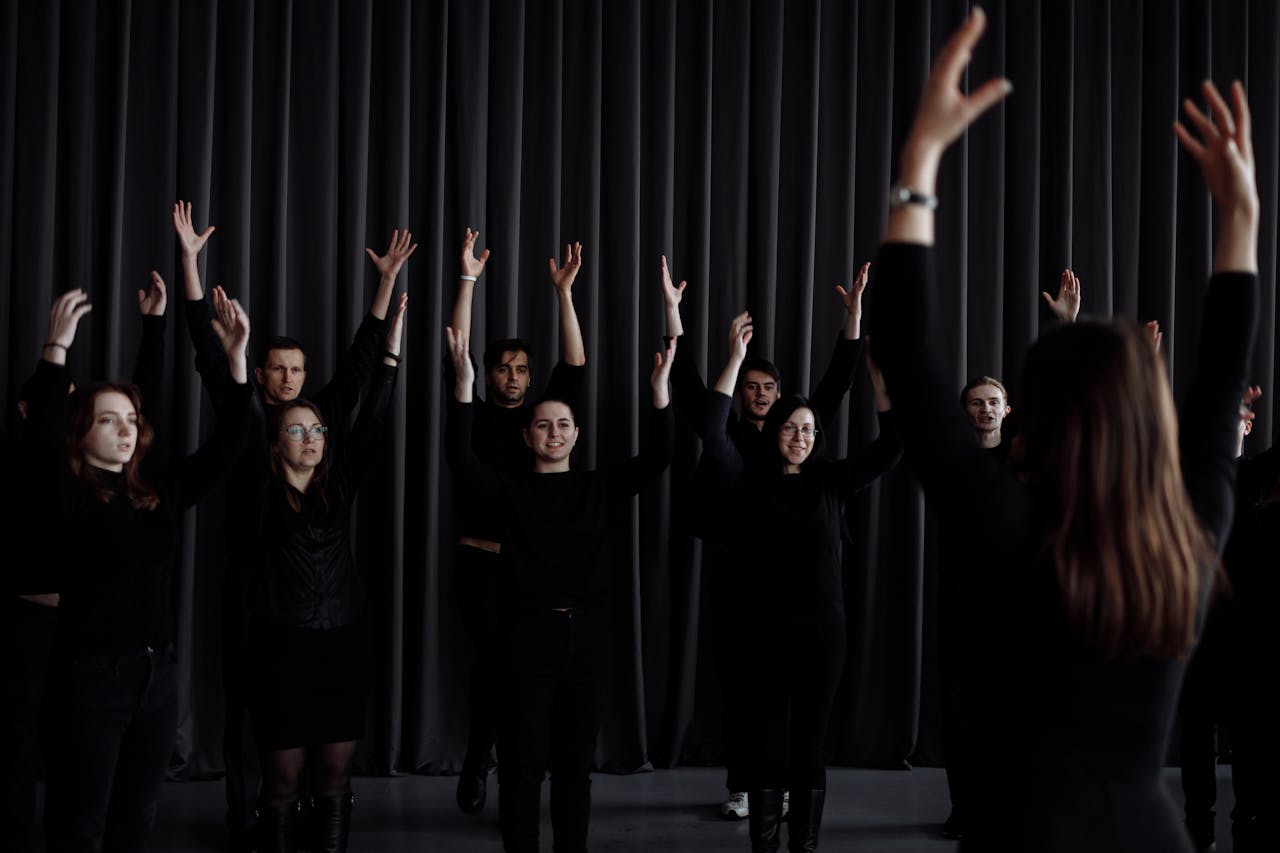 A group of performers practicing choreography with raised arms indoors.